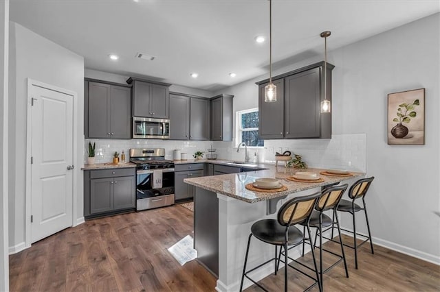 kitchen with decorative light fixtures, dark hardwood / wood-style floors, kitchen peninsula, gray cabinets, and stainless steel appliances