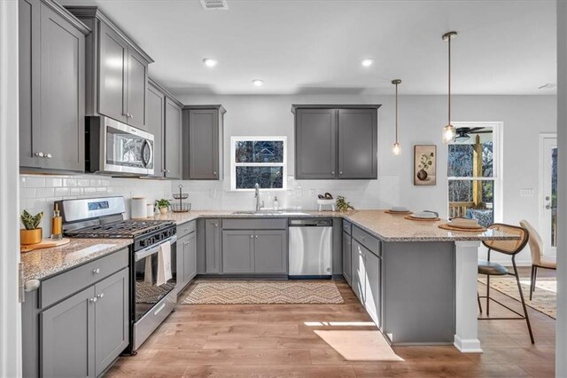 kitchen with a breakfast bar, appliances with stainless steel finishes, gray cabinetry, decorative light fixtures, and kitchen peninsula