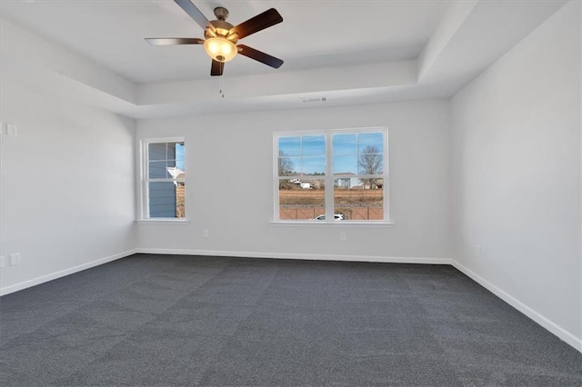 empty room featuring a raised ceiling, ceiling fan, plenty of natural light, and dark carpet