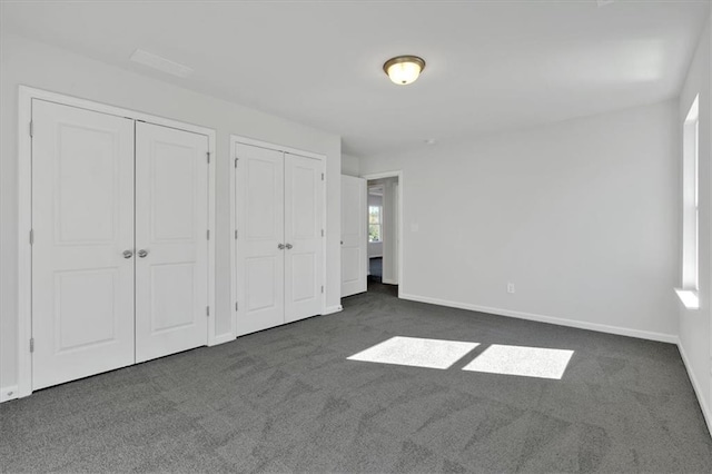 unfurnished bedroom featuring multiple closets and dark colored carpet