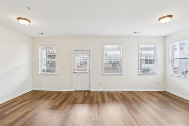 unfurnished room with baseboards, visible vents, a healthy amount of sunlight, and wood finished floors