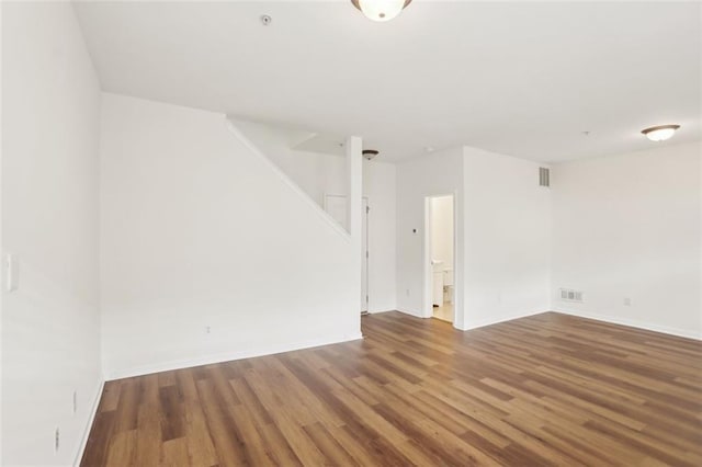 empty room with stairs, baseboards, visible vents, and wood finished floors