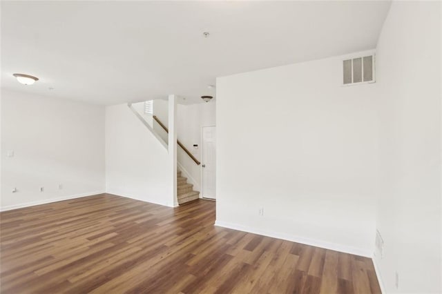 unfurnished room featuring stairway, baseboards, wood finished floors, and visible vents