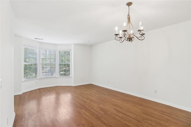 spare room with visible vents, baseboards, wood finished floors, and a notable chandelier