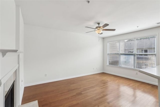 unfurnished living room with baseboards, a fireplace with flush hearth, ceiling fan, and wood finished floors