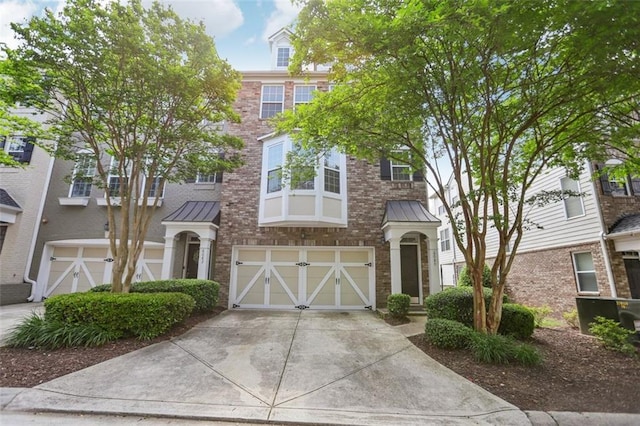 townhome / multi-family property with a standing seam roof, driveway, metal roof, and a garage