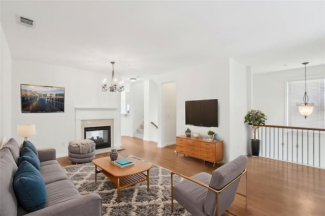 living room with visible vents, stairs, wood finished floors, a chandelier, and a multi sided fireplace