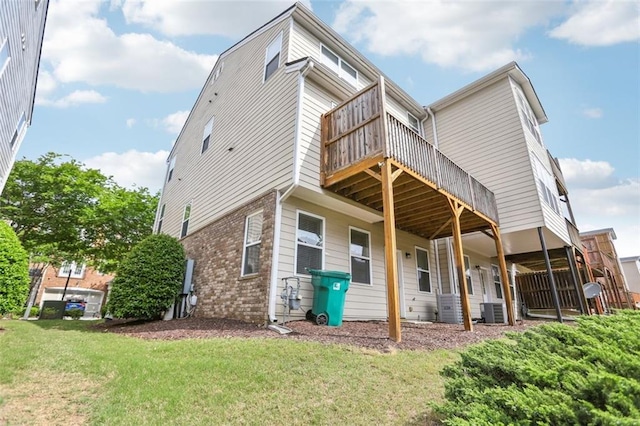rear view of property with central air condition unit, a wooden deck, a yard, and brick siding