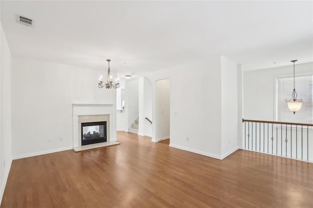 unfurnished living room featuring an inviting chandelier, a multi sided fireplace, baseboards, wood finished floors, and visible vents