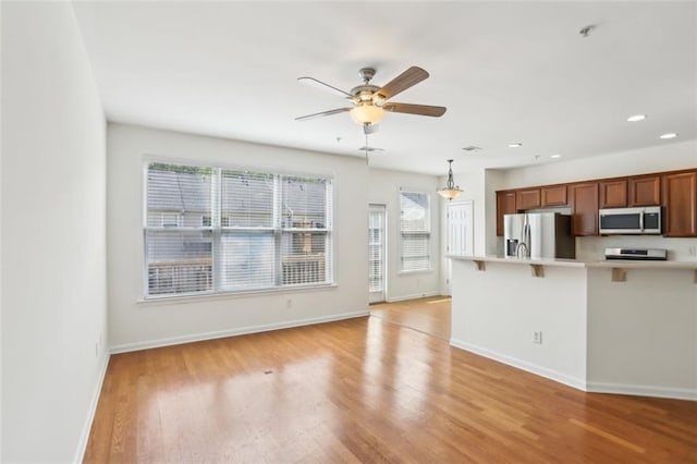 kitchen with a breakfast bar, light countertops, light wood-style flooring, stainless steel appliances, and baseboards