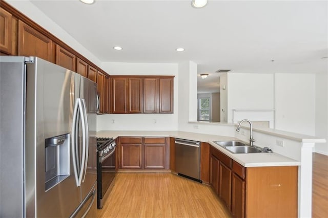 kitchen featuring a peninsula, appliances with stainless steel finishes, a sink, and light wood finished floors