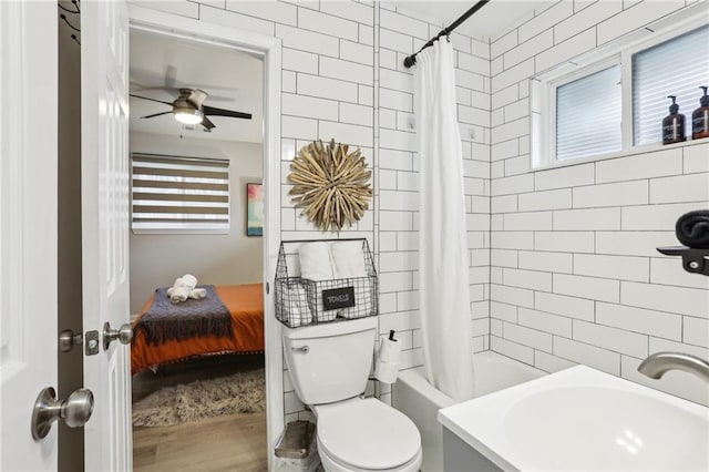 ensuite bathroom featuring toilet, shower / bath combo with shower curtain, ceiling fan, a sink, and wood finished floors