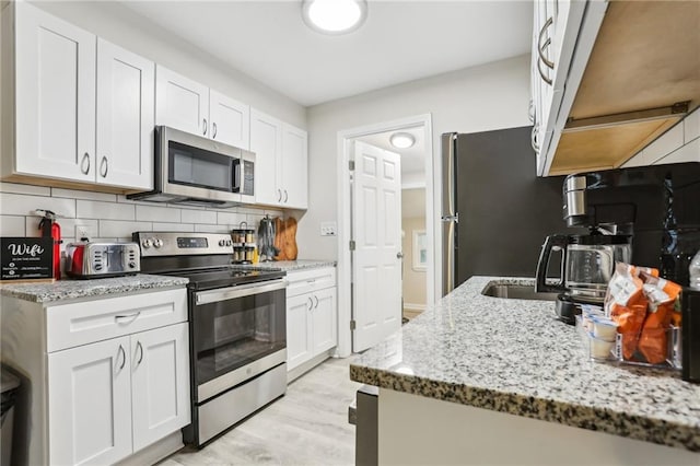 kitchen featuring stainless steel appliances, backsplash, light wood-style floors, white cabinets, and light stone countertops