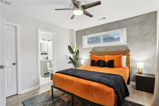 bedroom with baseboards, visible vents, ensuite bath, and wood finished floors