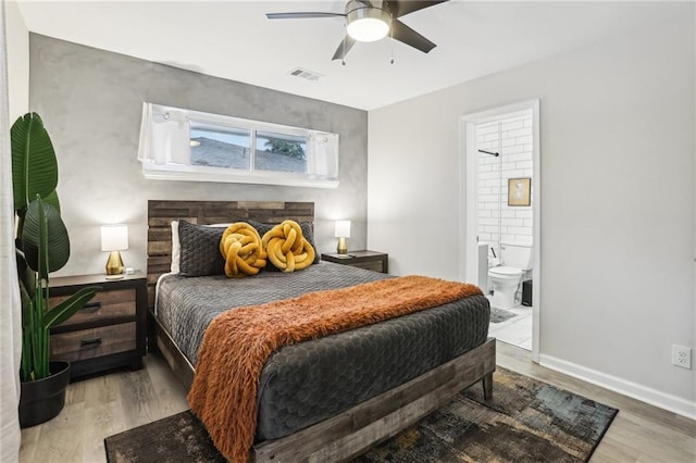 bedroom with wood finished floors, a ceiling fan, visible vents, baseboards, and ensuite bath