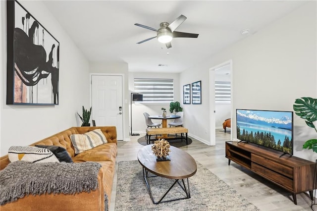 living room with light wood-type flooring, visible vents, baseboards, and a ceiling fan