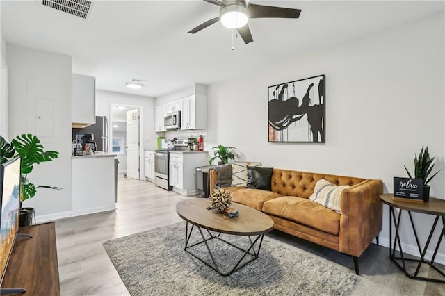 living area with light wood-style flooring, visible vents, ceiling fan, and baseboards