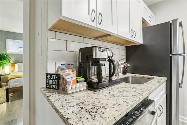 kitchen featuring backsplash, freestanding refrigerator, white cabinetry, a sink, and light stone countertops