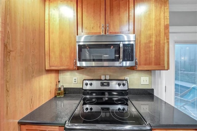 kitchen featuring crown molding, appliances with stainless steel finishes, dark stone countertops, and decorative backsplash