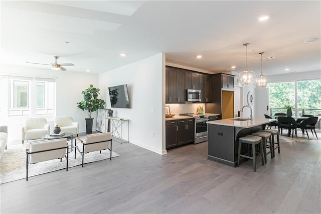 kitchen with a breakfast bar area, appliances with stainless steel finishes, hanging light fixtures, dark brown cabinets, and a center island with sink