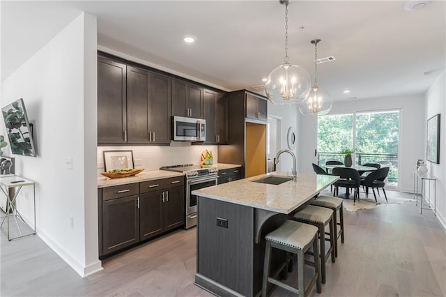 kitchen featuring decorative light fixtures, sink, a kitchen island with sink, stainless steel appliances, and light stone countertops