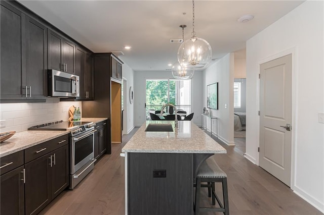 kitchen with light stone counters, sink, an island with sink, and appliances with stainless steel finishes