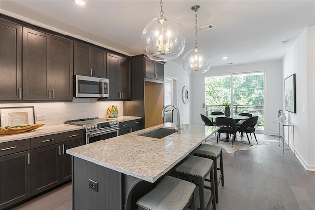 kitchen featuring dark brown cabinetry, sink, an island with sink, and appliances with stainless steel finishes