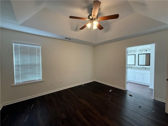 unfurnished room with ceiling fan, a sink, dark wood finished floors, a raised ceiling, and baseboards