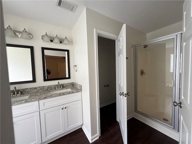 full bath with wood finished floors, a shower stall, double vanity, and baseboards
