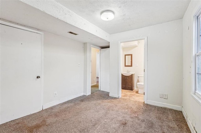unfurnished bedroom with a sink, baseboards, visible vents, ensuite bath, and carpet floors