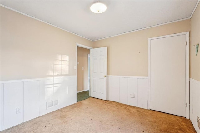 unfurnished bedroom featuring crown molding, visible vents, carpet flooring, and a wainscoted wall