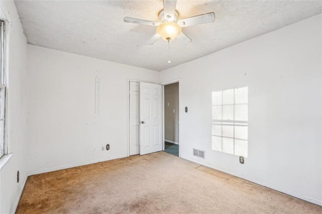 carpeted empty room with a textured ceiling, visible vents, baseboards, and ceiling fan