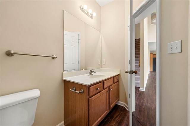 half bath featuring baseboards, vanity, toilet, and wood finished floors