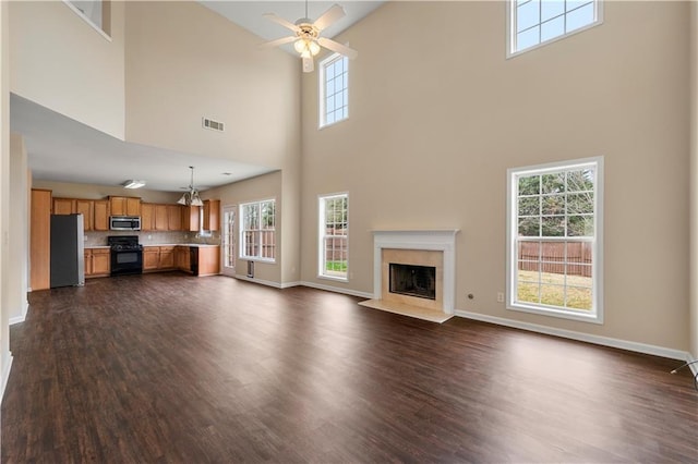 unfurnished living room featuring a premium fireplace, dark wood finished floors, visible vents, and baseboards