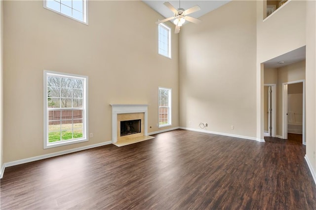 unfurnished living room featuring baseboards, dark wood-type flooring, a premium fireplace, and a healthy amount of sunlight