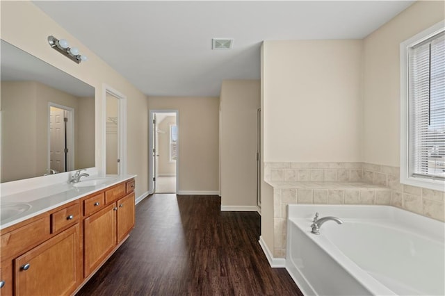 bathroom featuring a garden tub, wood finished floors, a sink, baseboards, and double vanity