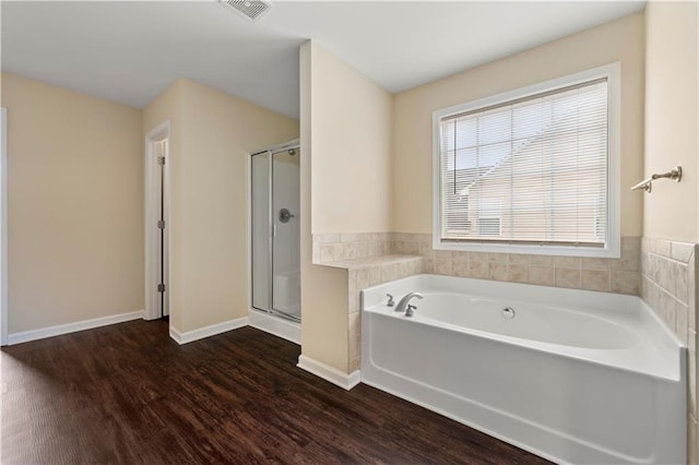 bathroom with a bath, a stall shower, wood finished floors, and visible vents