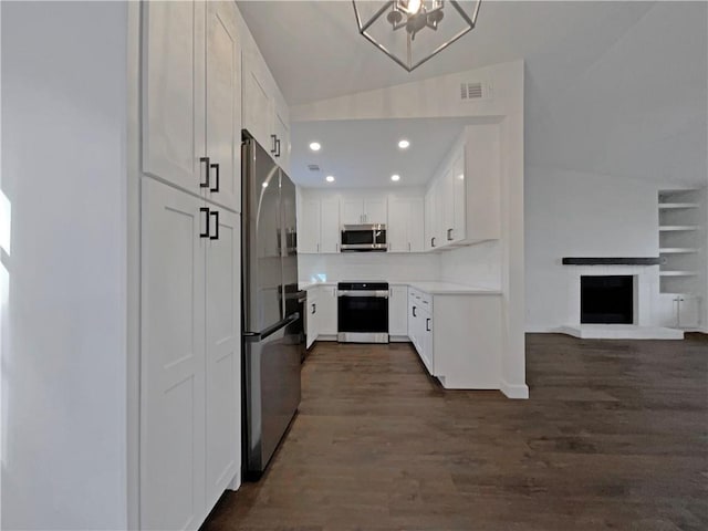 kitchen with lofted ceiling, white cabinets, appliances with stainless steel finishes, and dark wood-type flooring