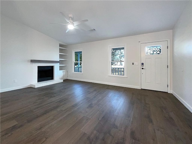 unfurnished living room featuring built in shelves, a brick fireplace, dark hardwood / wood-style flooring, and ceiling fan