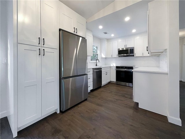 kitchen featuring dark wood-type flooring, white cabinets, backsplash, and appliances with stainless steel finishes