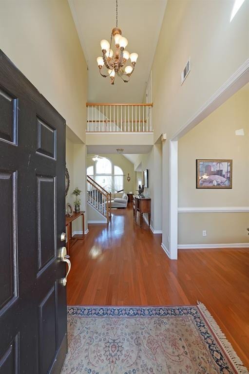 foyer with baseboards, visible vents, stairway, wood finished floors, and a notable chandelier