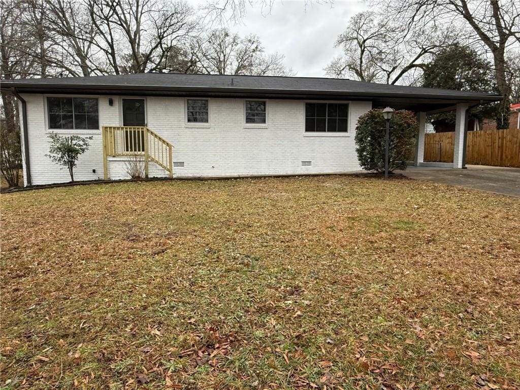 rear view of house with brick siding, an attached carport, fence, and a lawn