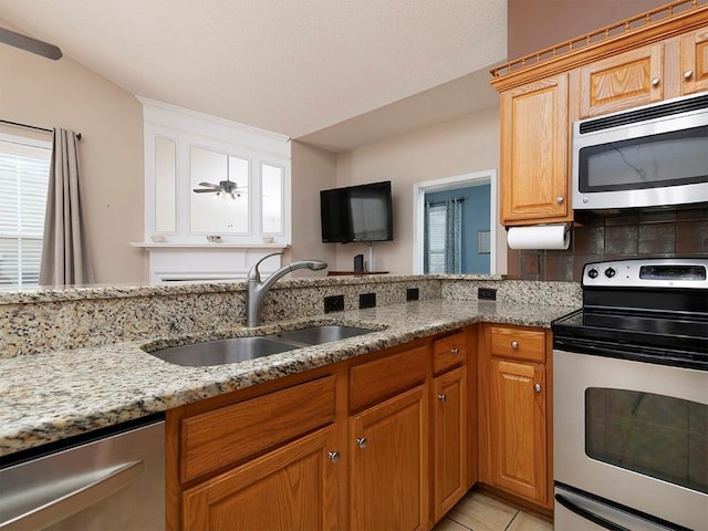 kitchen with ceiling fan, sink, stainless steel appliances, light stone counters, and light tile patterned flooring