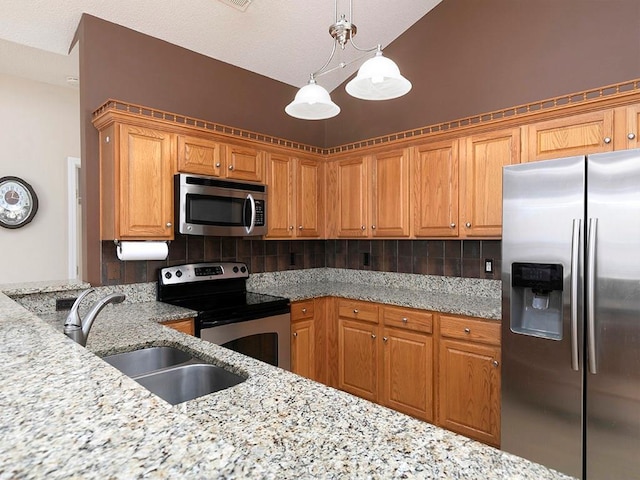 kitchen with hanging light fixtures, light stone countertops, sink, and appliances with stainless steel finishes