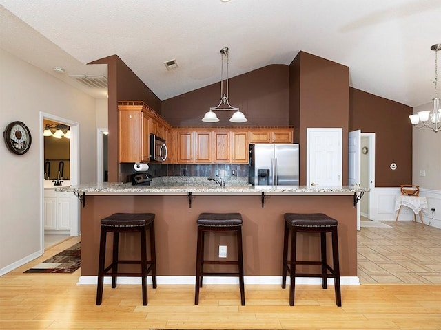 kitchen with a breakfast bar area, an inviting chandelier, stainless steel appliances, and light wood-type flooring