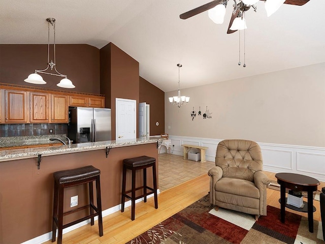 kitchen with light stone countertops, stainless steel fridge, tasteful backsplash, light hardwood / wood-style flooring, and a breakfast bar area