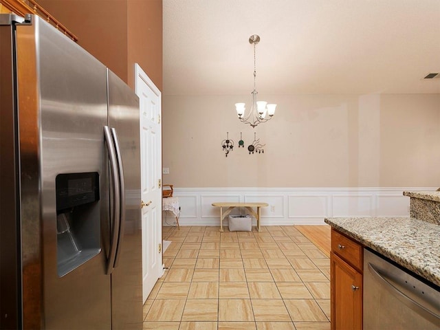 kitchen featuring pendant lighting, stainless steel appliances, light stone counters, and a notable chandelier