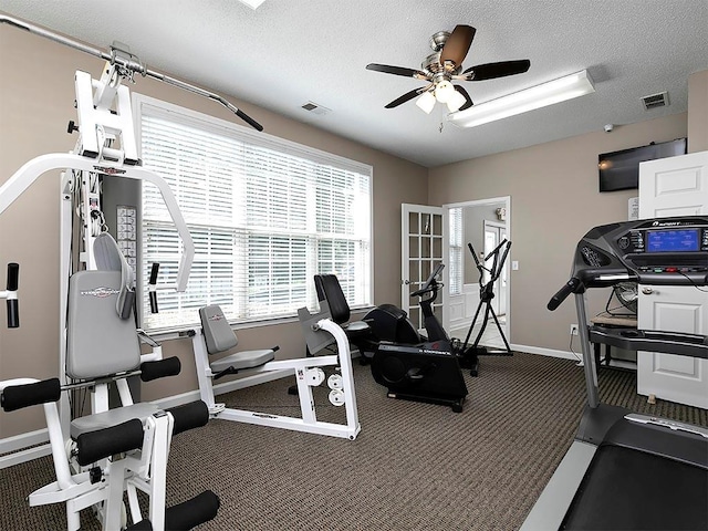 exercise area featuring dark colored carpet, ceiling fan, and a textured ceiling