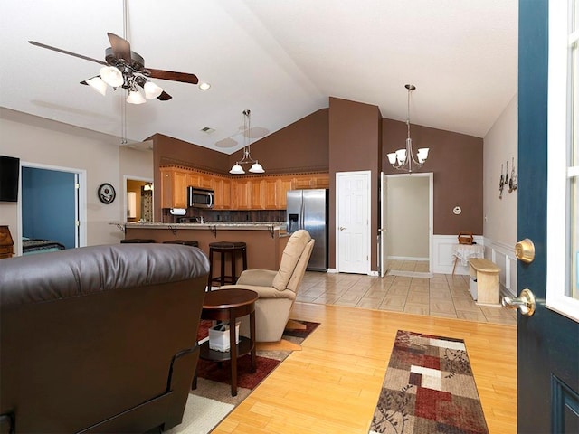 living room with light hardwood / wood-style flooring, high vaulted ceiling, and ceiling fan with notable chandelier