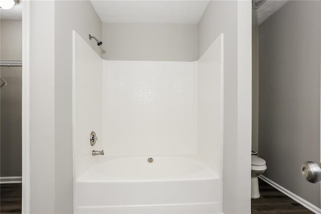 bathroom with toilet, wood finished floors, shower / bath combination, a textured ceiling, and baseboards